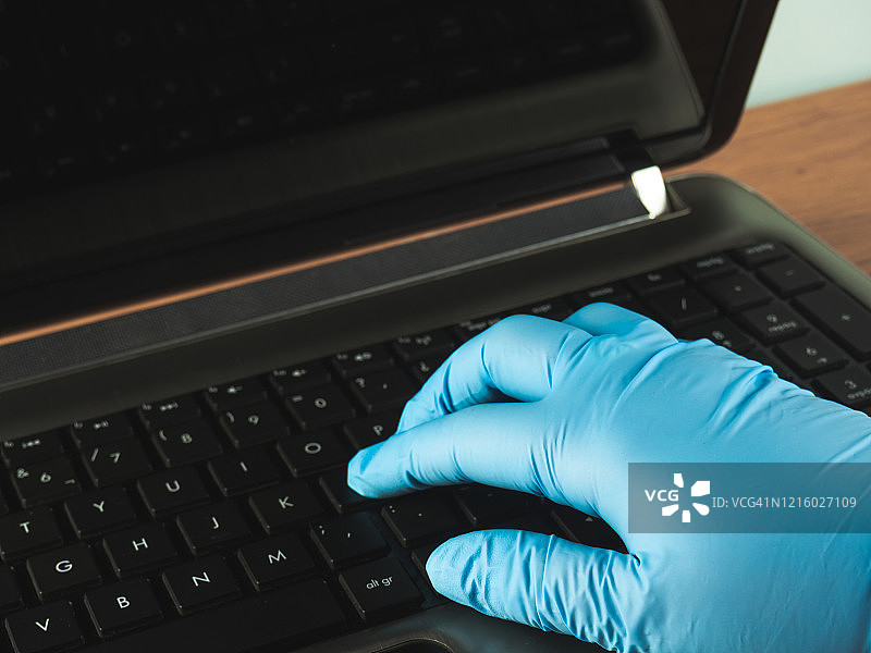 在家使用笔记本电脑和丁腈防护手套工作的人图片素材