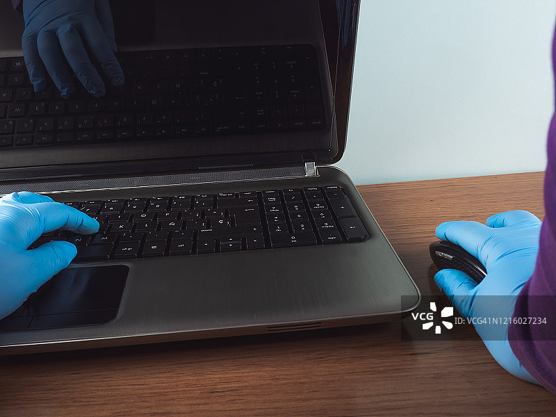 戴着丁腈防护手套，在家用笔记本电脑和鼠标工作的人图片素材