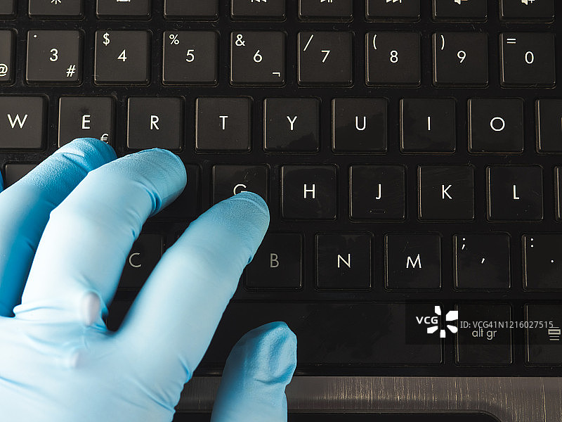 在家使用笔记本电脑和丁腈防护手套工作的人图片素材