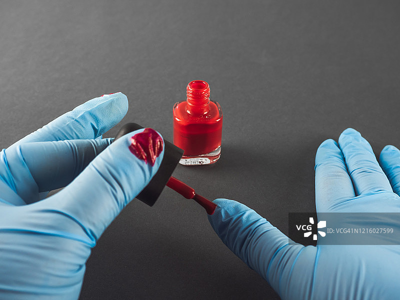 一个人在腈纶防护手套上用红色珐琅涂指甲图片素材