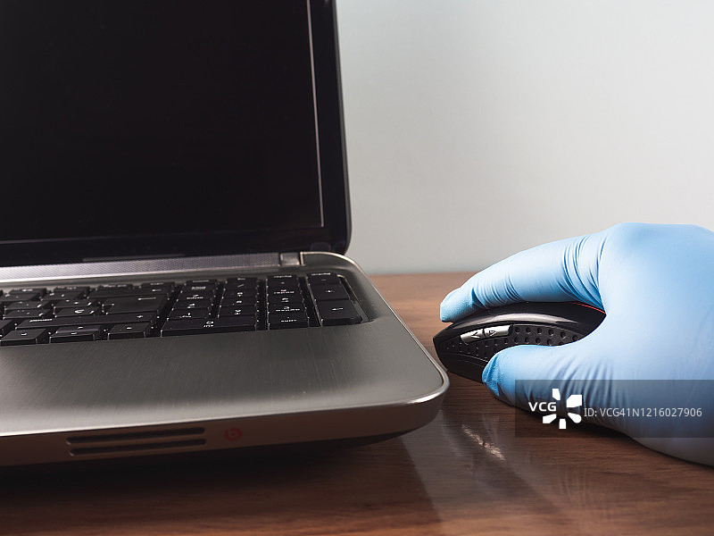 戴着丁腈防护手套，在家用笔记本电脑和鼠标工作的人图片素材