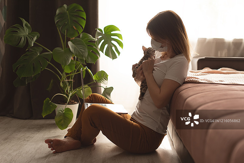 新冠病毒：戴防护口罩在家工作的年轻女商人，使用消毒凝胶图片素材