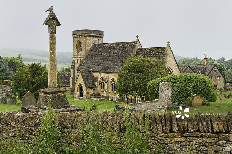 英格兰科茨沃尔德圣巴拿巴教堂墓地的战争纪念碑，有雾和雨图片素材