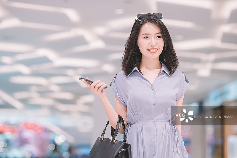 中国女性在购物中心购物，拿着智能手机和钱包图片素材