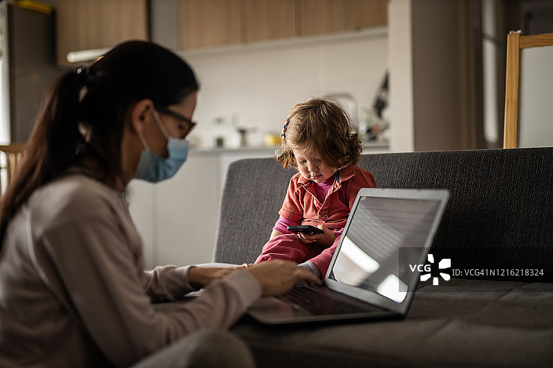 年轻女人在家用笔记本电脑工作，照顾女儿图片素材