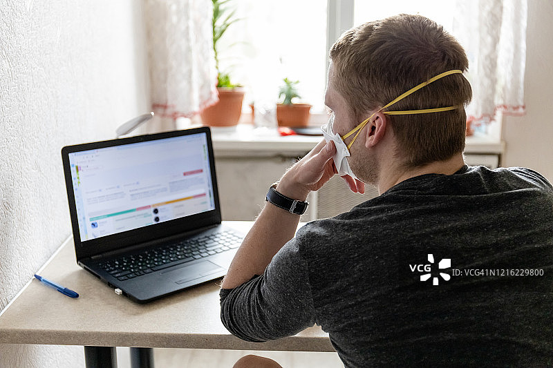 戴防护口罩的年轻男人，居家隔离用笔记本工作图片素材