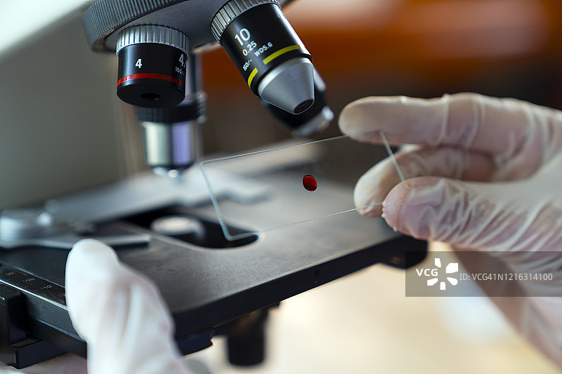 科研实验室中科学家在显微镜下放置载玻片的场景图片素材
