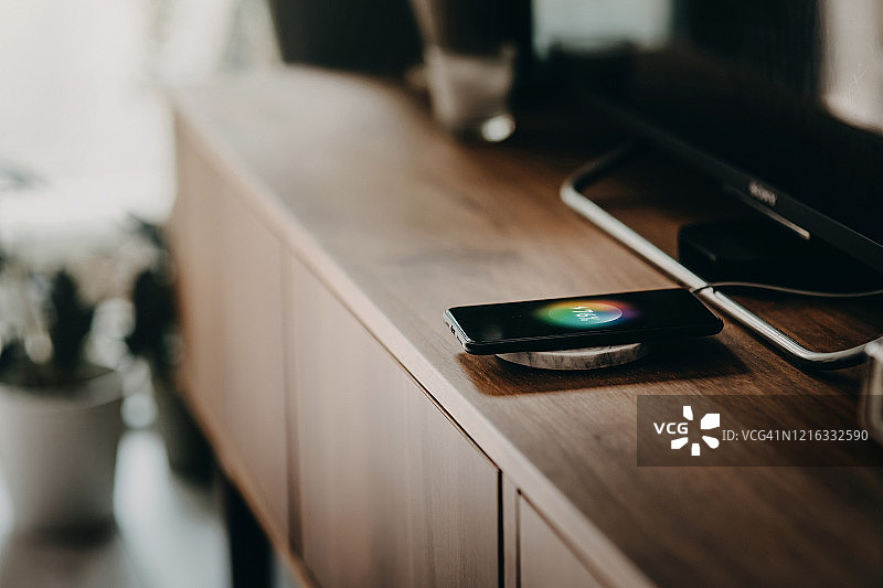 在客厅的柜子上使用无线充电设备为智能手机充电图片素材