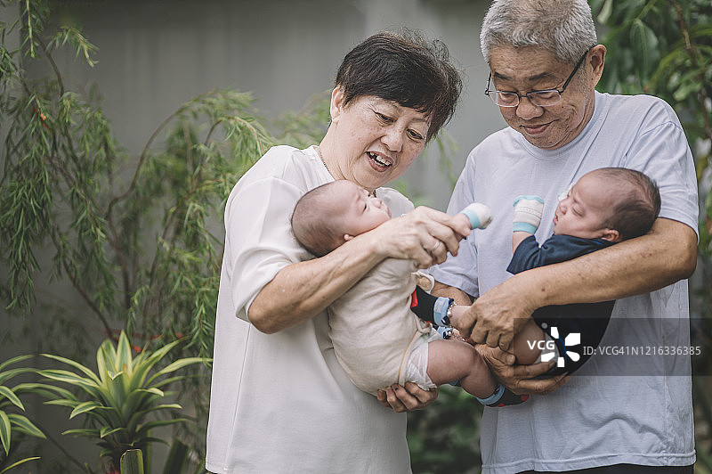亚洲华人多代同堂家庭在房子前院，祖父母抱着双胞胎男孙，享受亲情时光图片素材