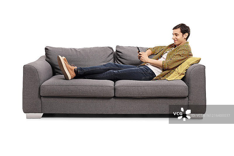 放松的年轻男人躺在沙发上玩手机图片素材