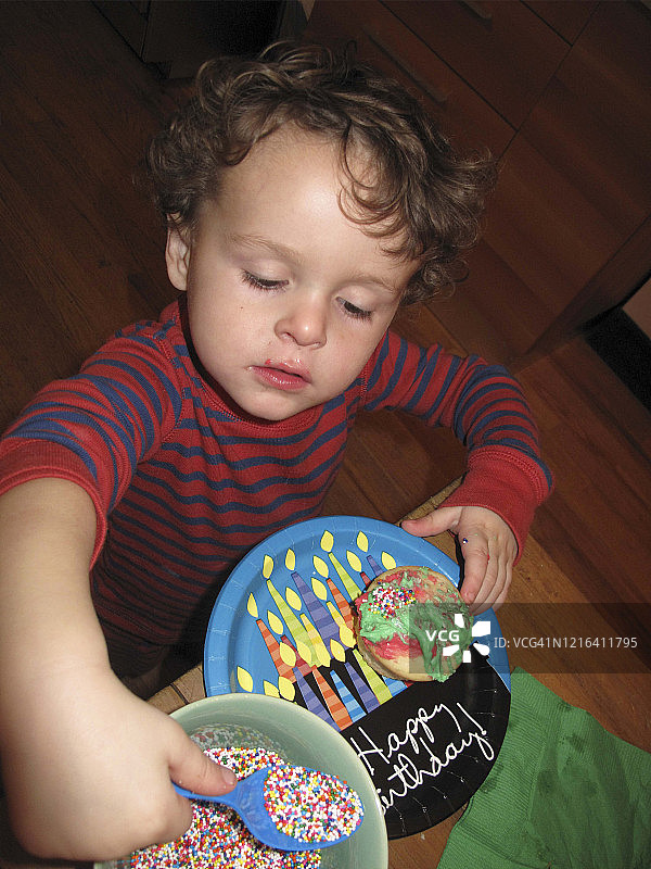 穿着睡衣的小男孩正在装饰纸杯蛋糕，嘴上沾着彩色糖霜图片素材