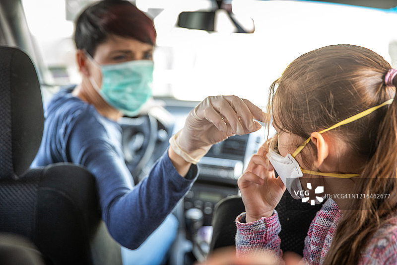 母亲在和女儿乘车离开前为她戴上防护口罩图片素材