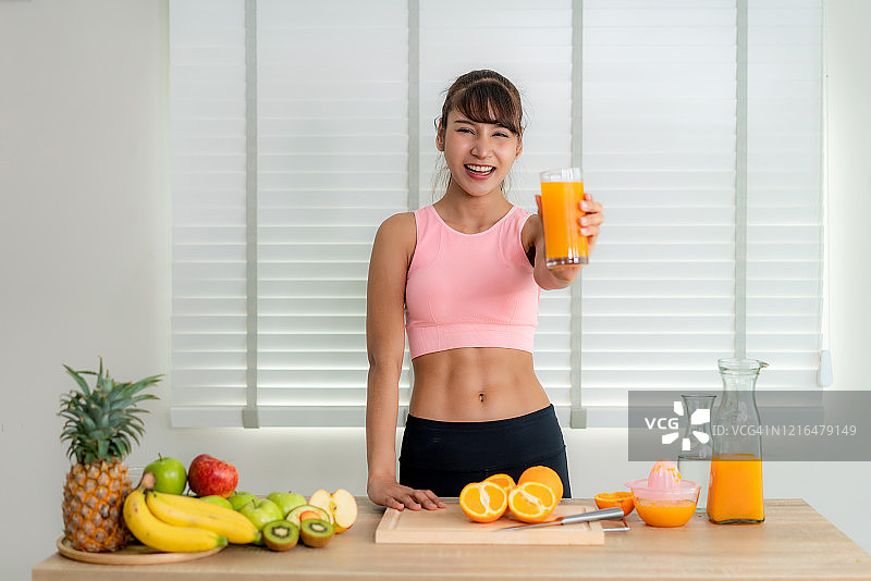穿着粉色运动装，在厨房榨橙汁的亚洲年轻美女图片素材
