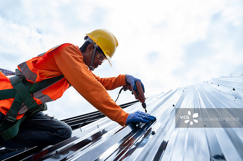 在新屋顶上拧螺丝的修理工图片素材
