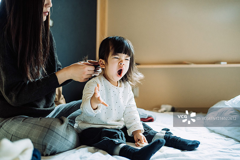 母亲在离家前为打哈欠的小女儿扎头发并穿衣服图片素材