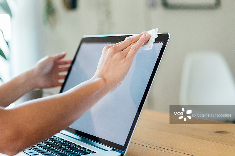女性用清洁湿巾擦拭笔记本电脑表面的特写图片素材
