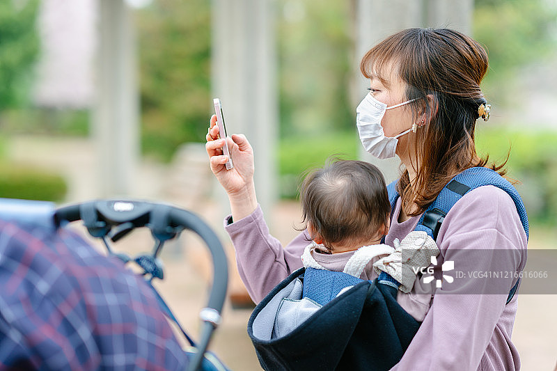 戴外科口罩的母亲抱宝宝玩手机图片素材