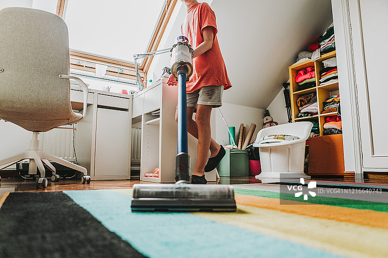 青少年男性在卧室使用真空吸尘器（局部）图片素材