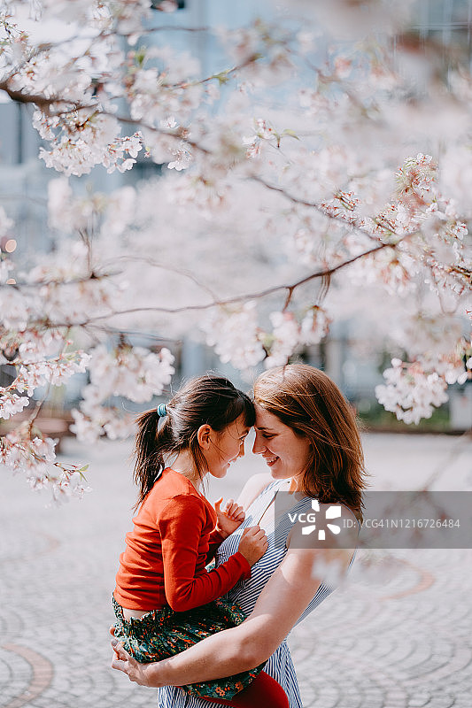 母亲在东京樱花树下抱着小女孩图片素材