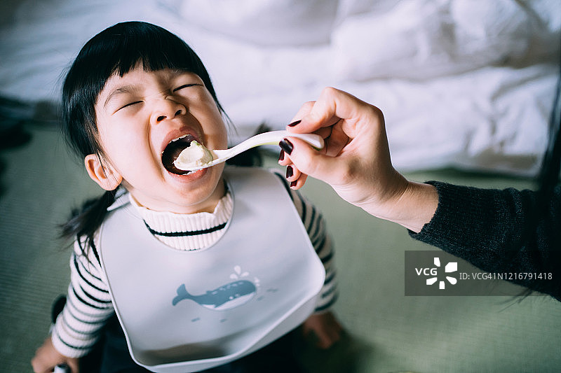 快乐的年轻亚洲母亲在家给小女儿喂新鲜鳄梨图片素材