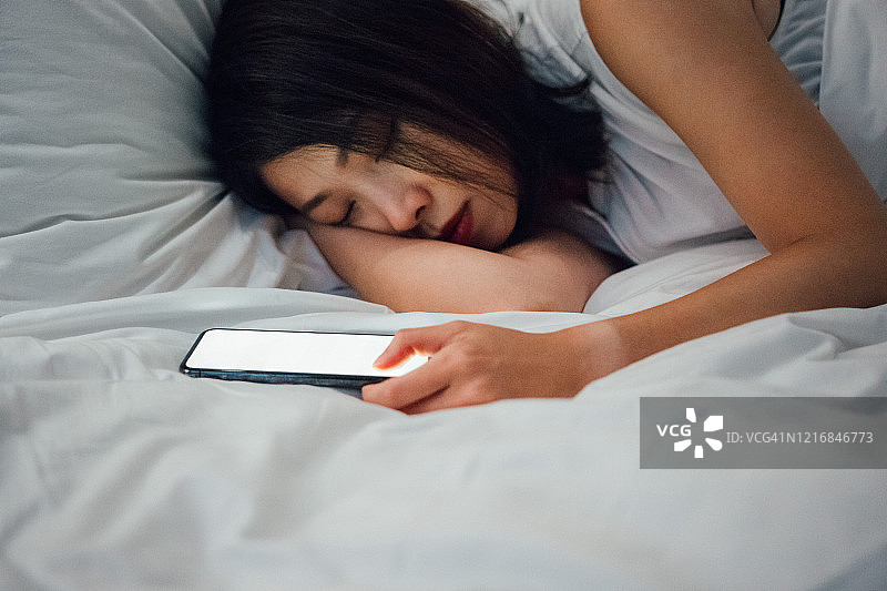 年轻女子在床上睡着，旁边放着智能手机图片素材