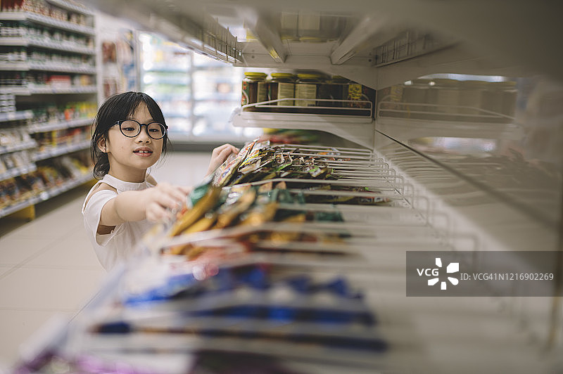 在中国超市里，年轻女孩从货架上挑选商品图片素材