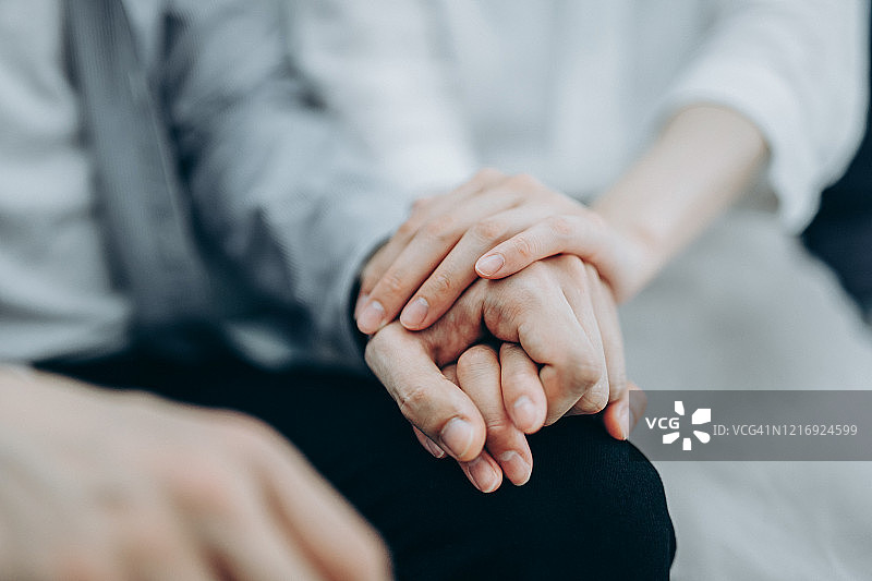 疫情期间，年轻夫妇在自我隔离期间坐在沙发上，充满同情地握着手图片素材