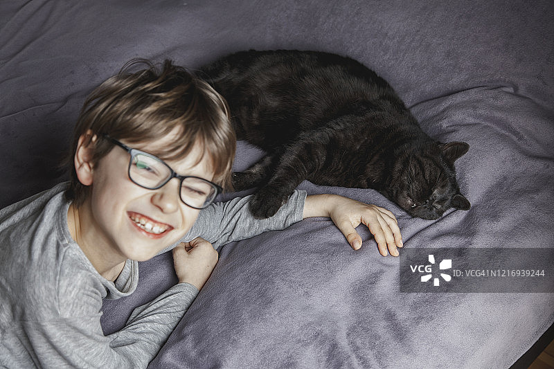在床上和猫一起微笑的男孩图片素材