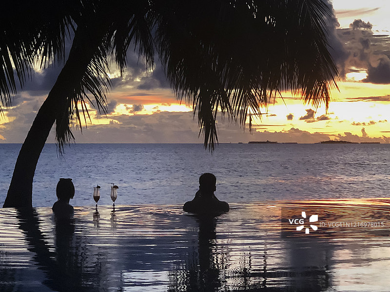 棕榈树下情侣剪影的无边泳池热带日落图片素材