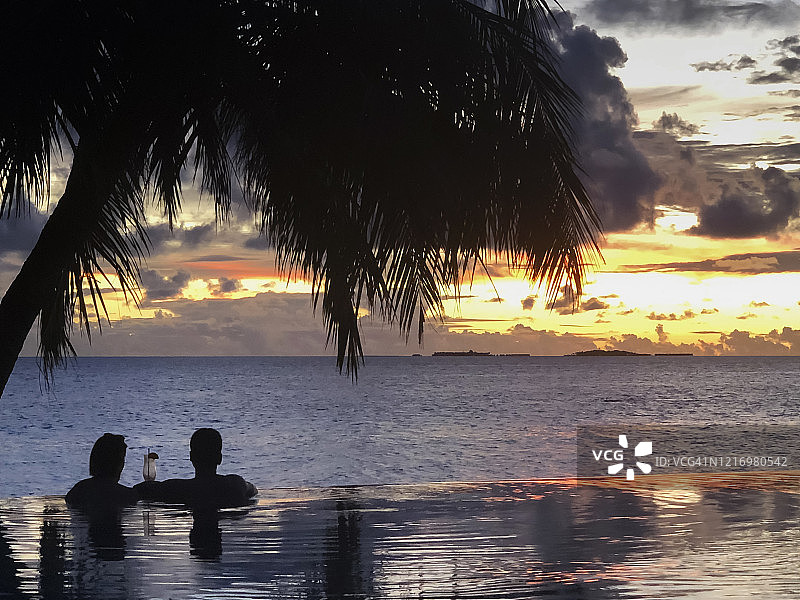 热带日落，棕榈树下情侣剪影与无边泳池图片素材