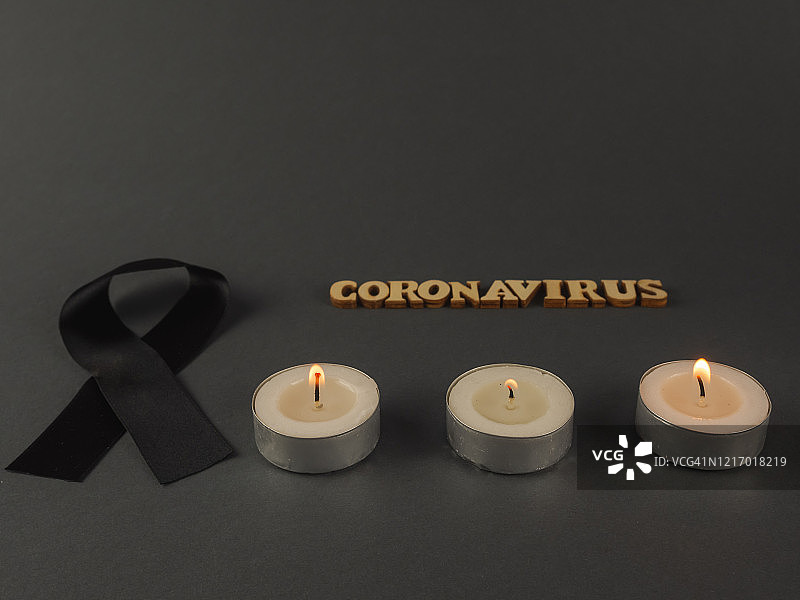 燃烧的蜡烛、黑色哀悼丝带和木制字母拼写的“新型冠状病毒”图片素材