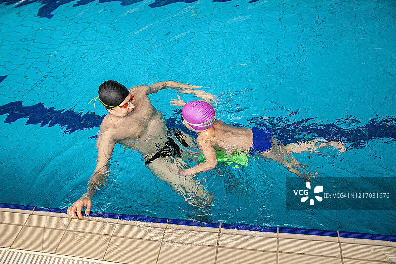 父亲教儿子在游泳池里练习蛙泳图片素材