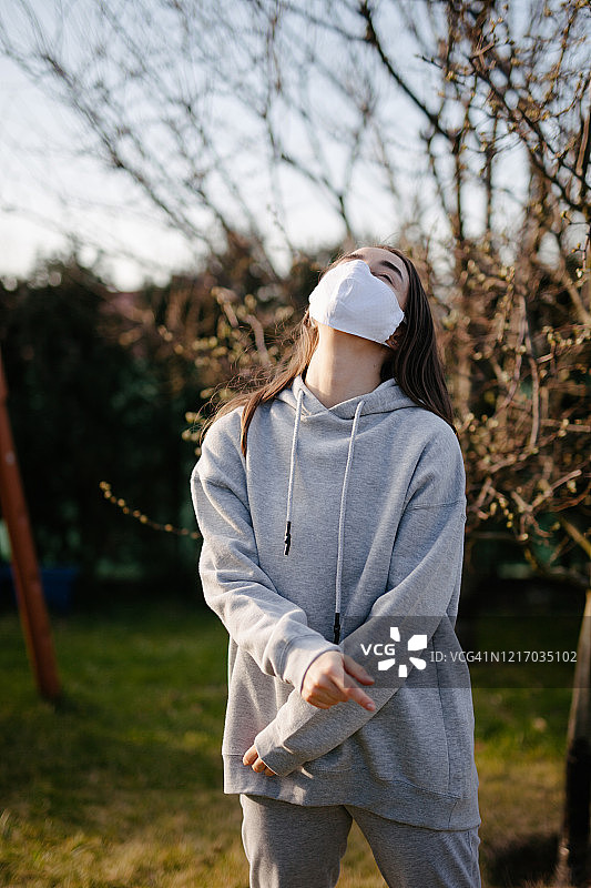 在自家后院戴着口罩向上看的年轻女人图片素材