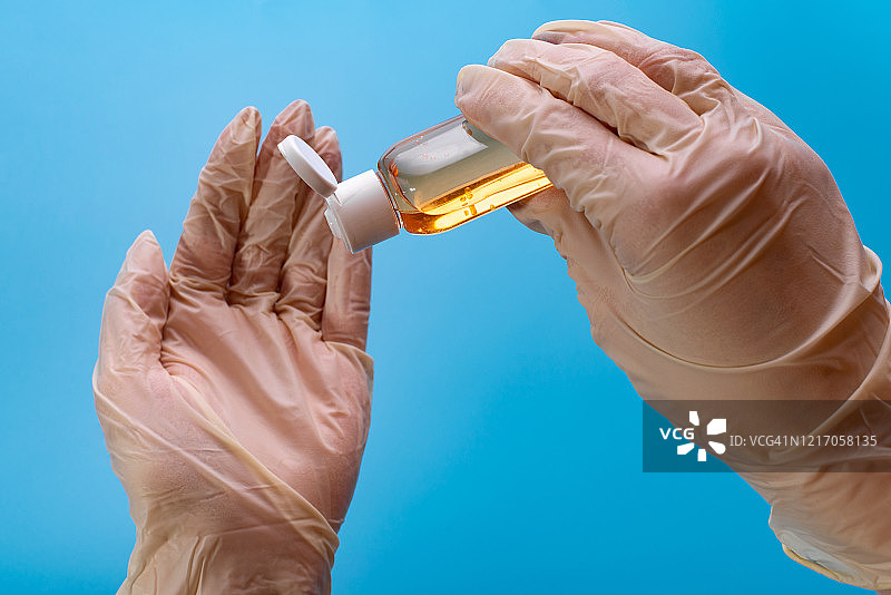 戴手套使用消毒剂。医生在蓝色手套中使用消毒剂图片素材