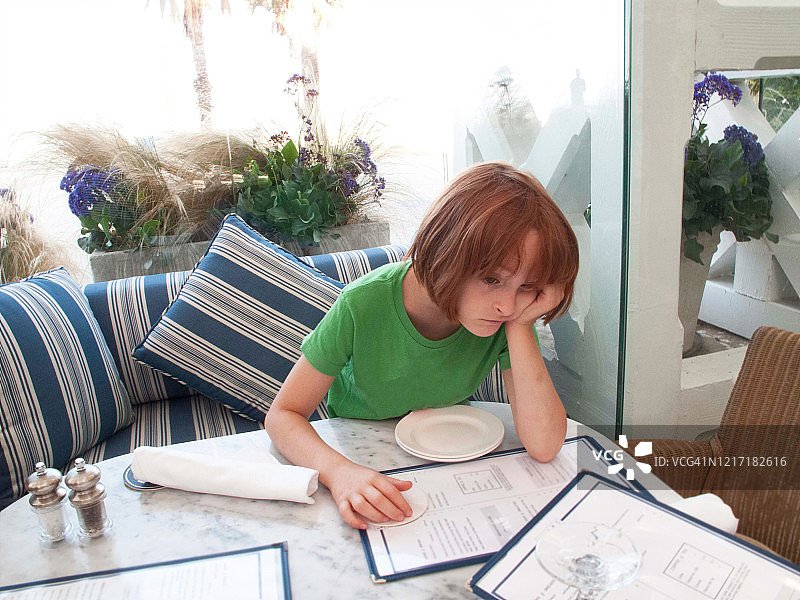 独自坐在咖啡馆靠窗边，感到无聊的红发小女孩图片素材