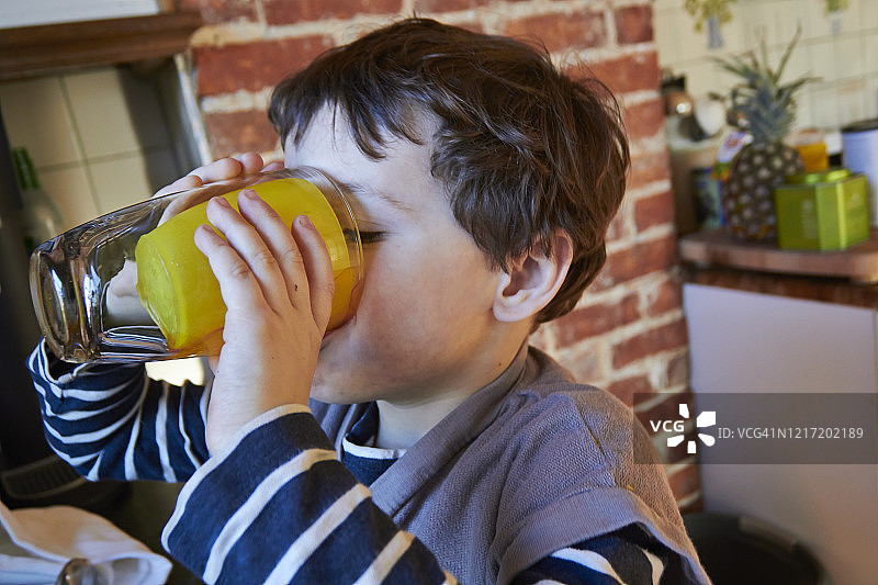 喝杯装果汁的棕色卷发棕色眼睛小男孩图片素材