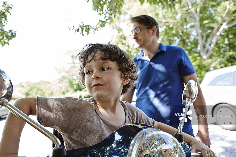 少年坐在父亲的摩托车上，看向远方图片素材
