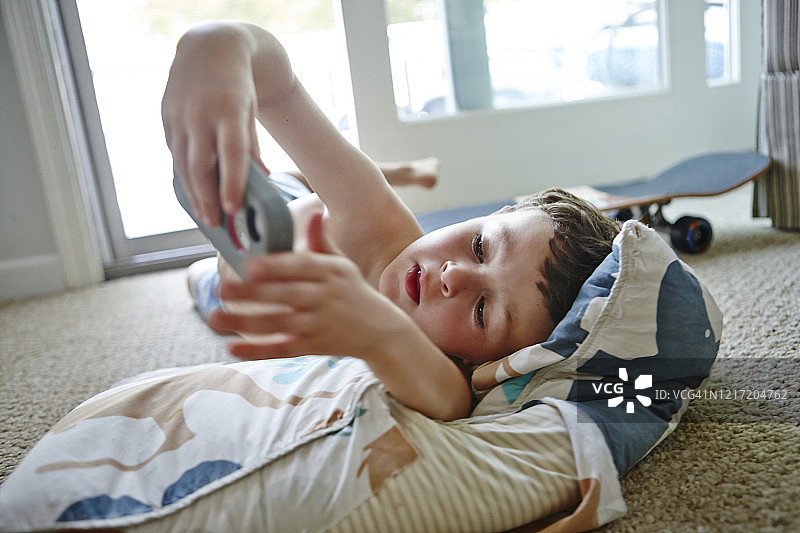 穿泳裤的棕色卷发小男孩趴着看手机图片素材