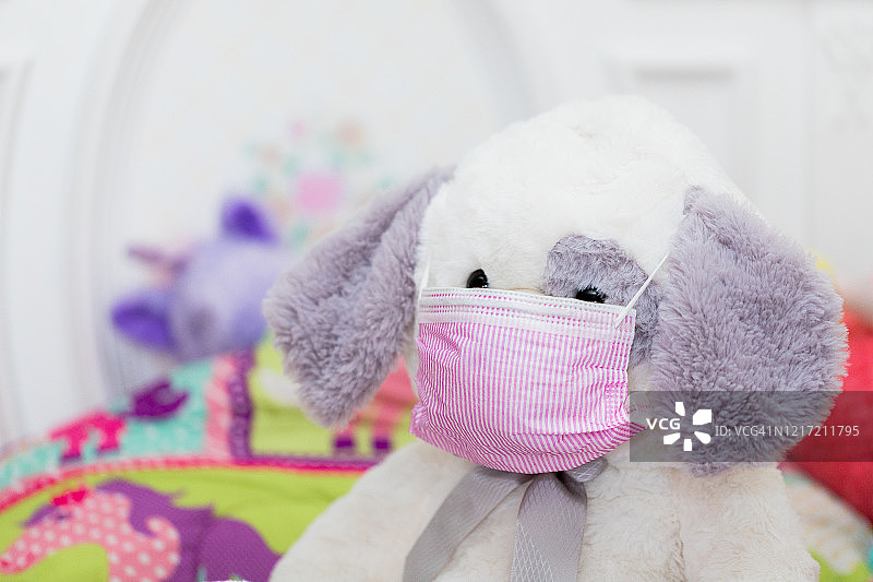 可爱的白色毛绒小狗，灰色耳朵和粉红色口罩，在女孩的床上练习保持社交距离图片素材