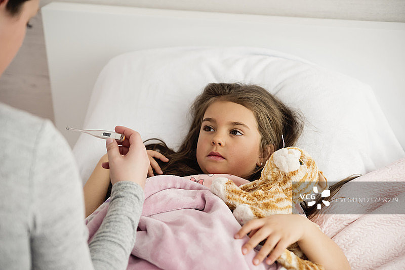 生病的小女孩躺在床上，妈妈拿着体温计图片素材