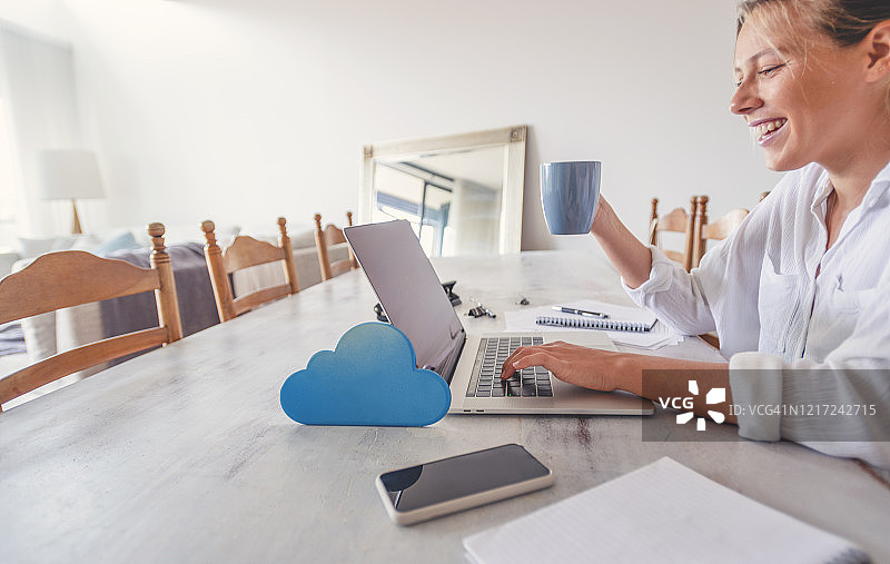 女人在家工作时使用带有云图标的笔记本电脑图片素材