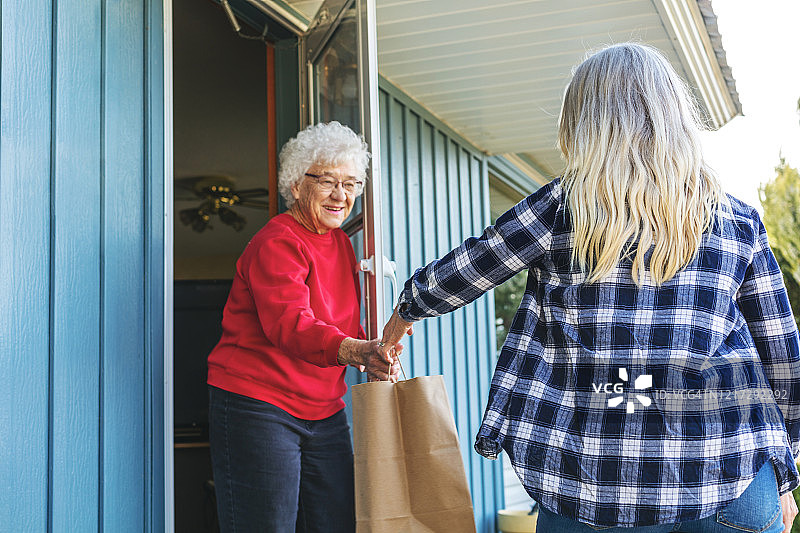 疫情期间中年女人送杂货给老年女人保持社交距离图片素材