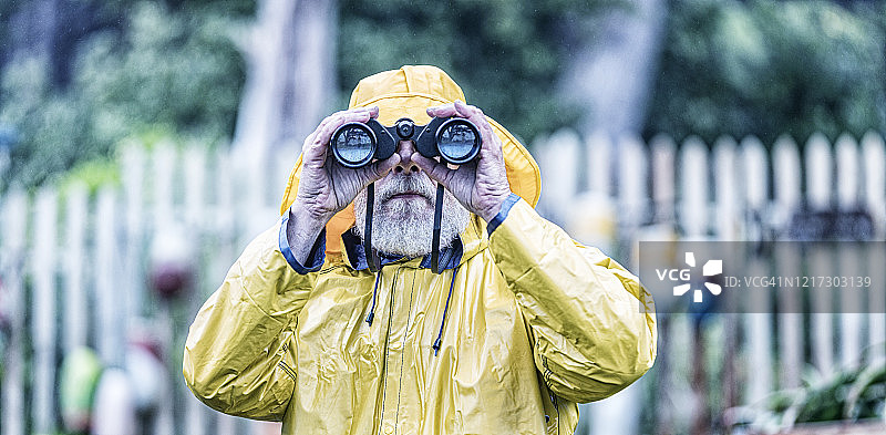 穿黄色雨衣的水手用双筒望远镜看镜头图片素材