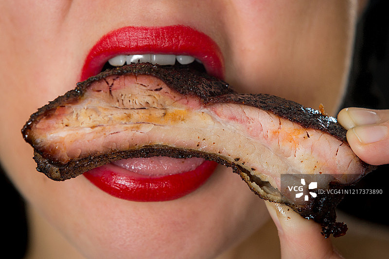 涂着口红的女人吃烤排骨图片素材