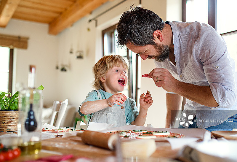 年长的父亲和小儿子在家做披萨，烹饪图片素材