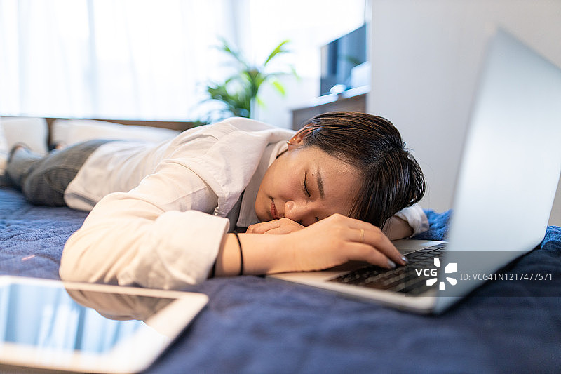 年轻女子在床上使用笔记本电脑时睡着了图片素材