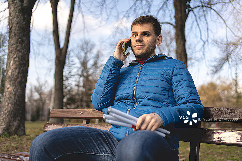年轻男人在户外拿着折叠盲杖打电话图片素材