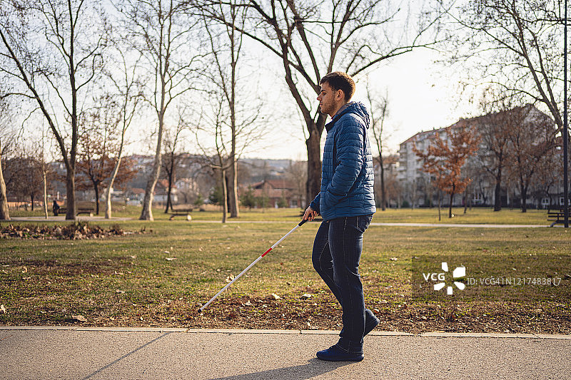 年轻盲人拄着盲杖在公园散步图片素材
