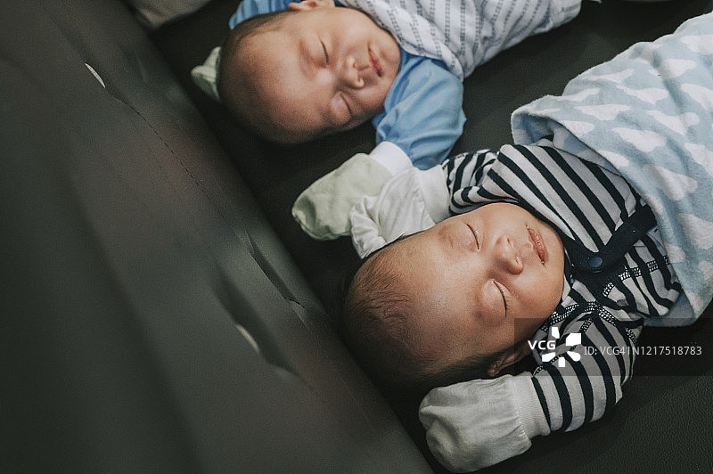 一对裹着毯子戴着手套在沙发上睡觉的亚洲中国男婴图片素材