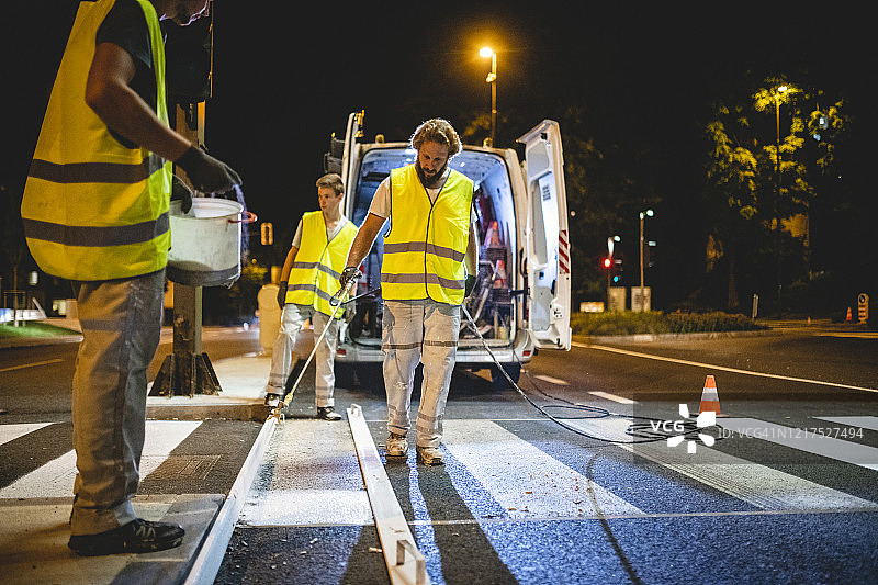 建筑工人在夜晚喷涂人行横道线图片素材